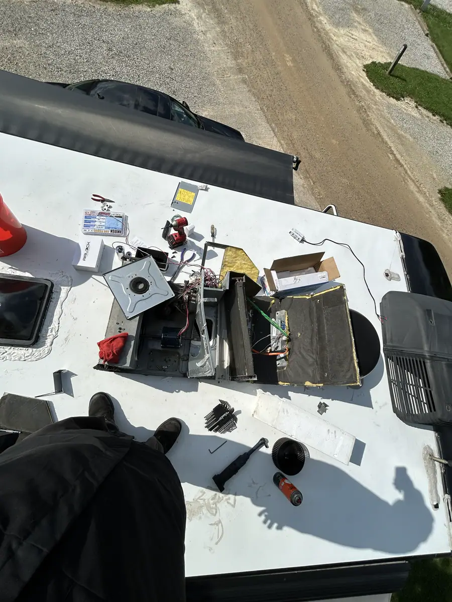 On-roof RV air conditioner repair in progress with tools and a Peplink networking box on the roof membrane.