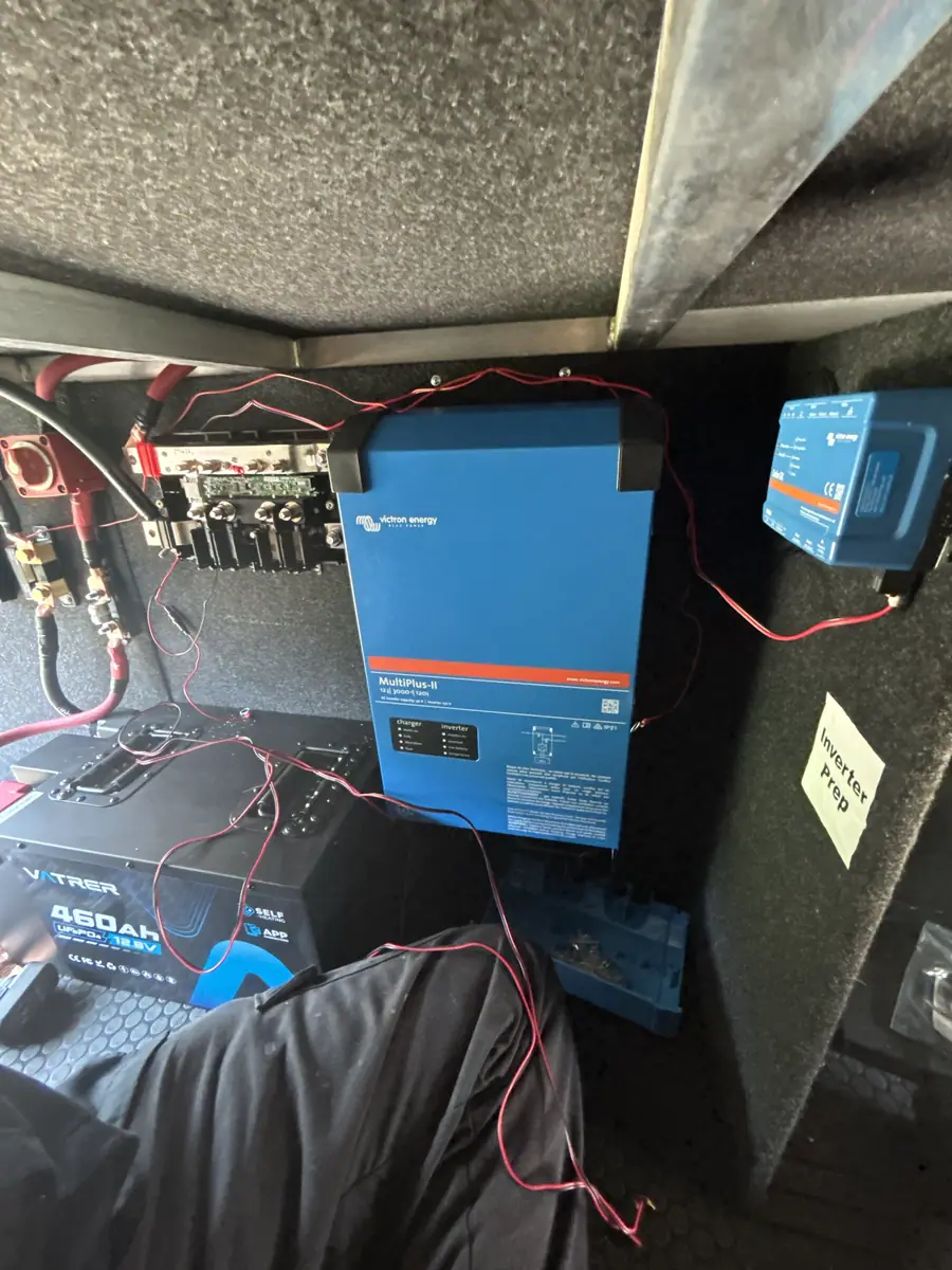 Technician installing a Victron MultiPlus-II and 460Ah lithium battery in an RV storage bay.